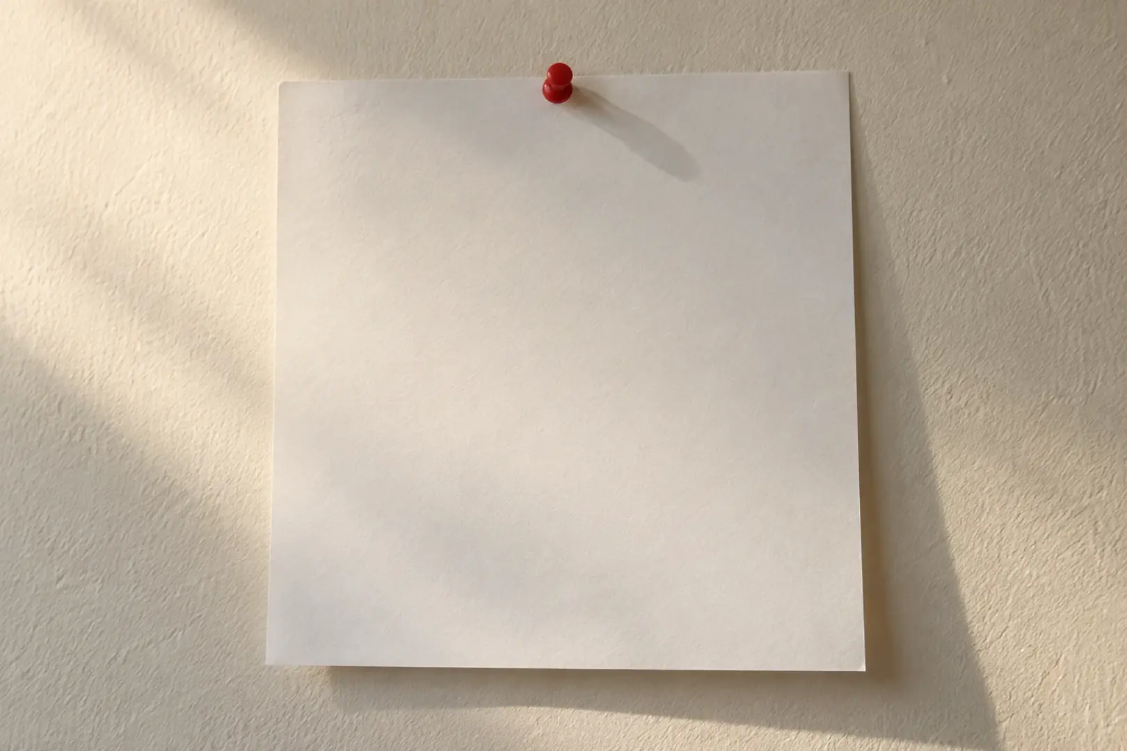 A blank calendar page pinned to a plain wall in raking afternoon light, Southern California interior