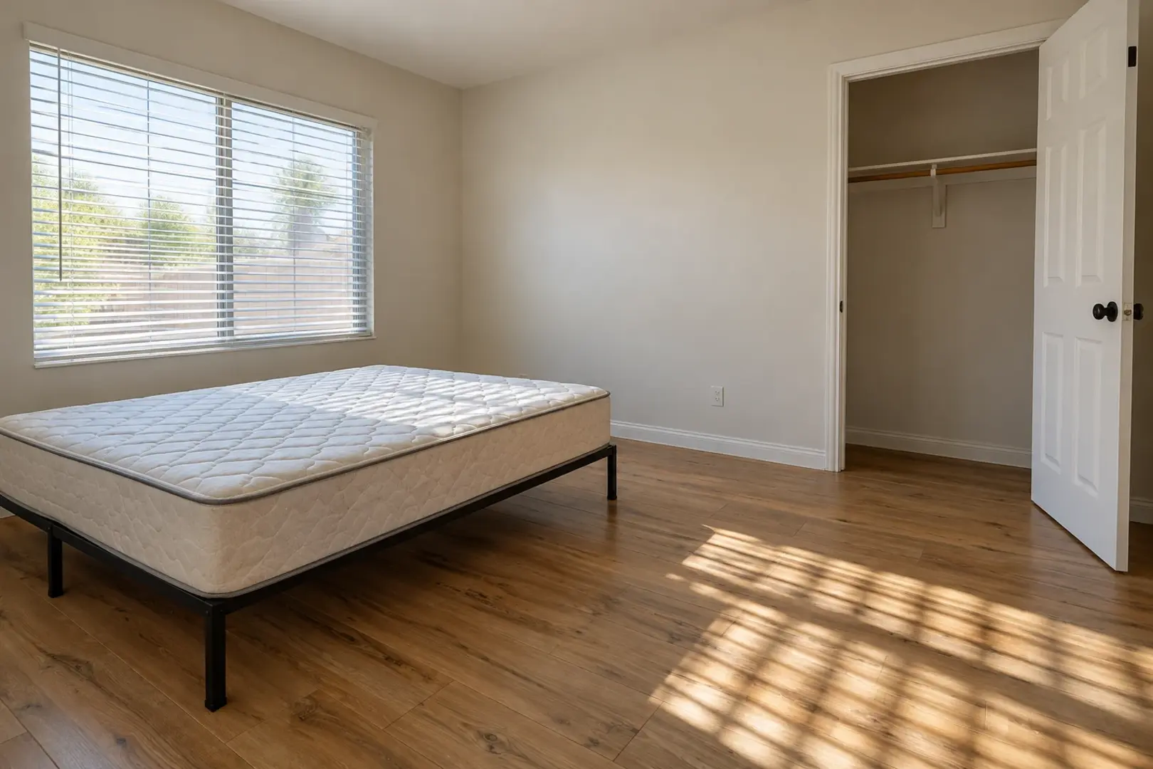 A bedroom stripped to a bare mattress with morning light through open blinds across a wood floor, Murrieta CA